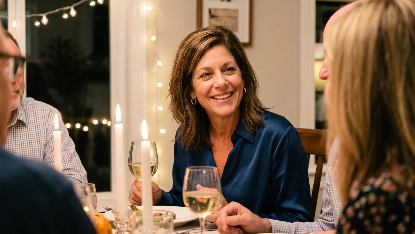 A woman smiling and composed at a dinner party, wine glass in hand, looking completely put together