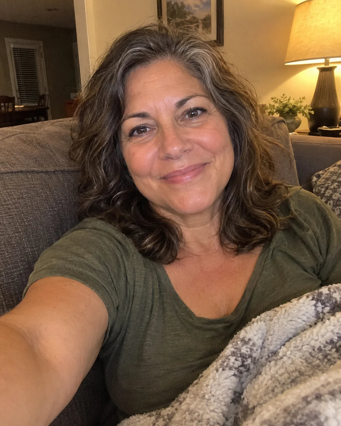 Woman relaxed on her couch in the evening, smiling, phone held at arm's length