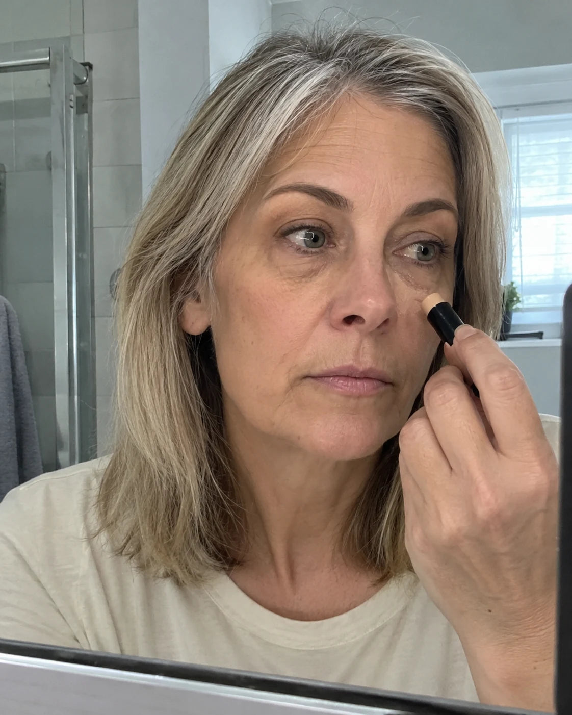 Woman applying concealer in a bathroom mirror