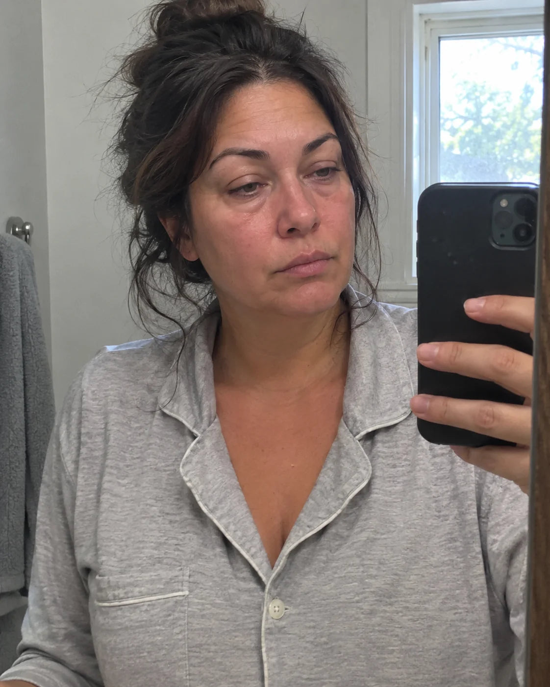 A tired woman looking at her puffy face in the bathroom mirror in the morning