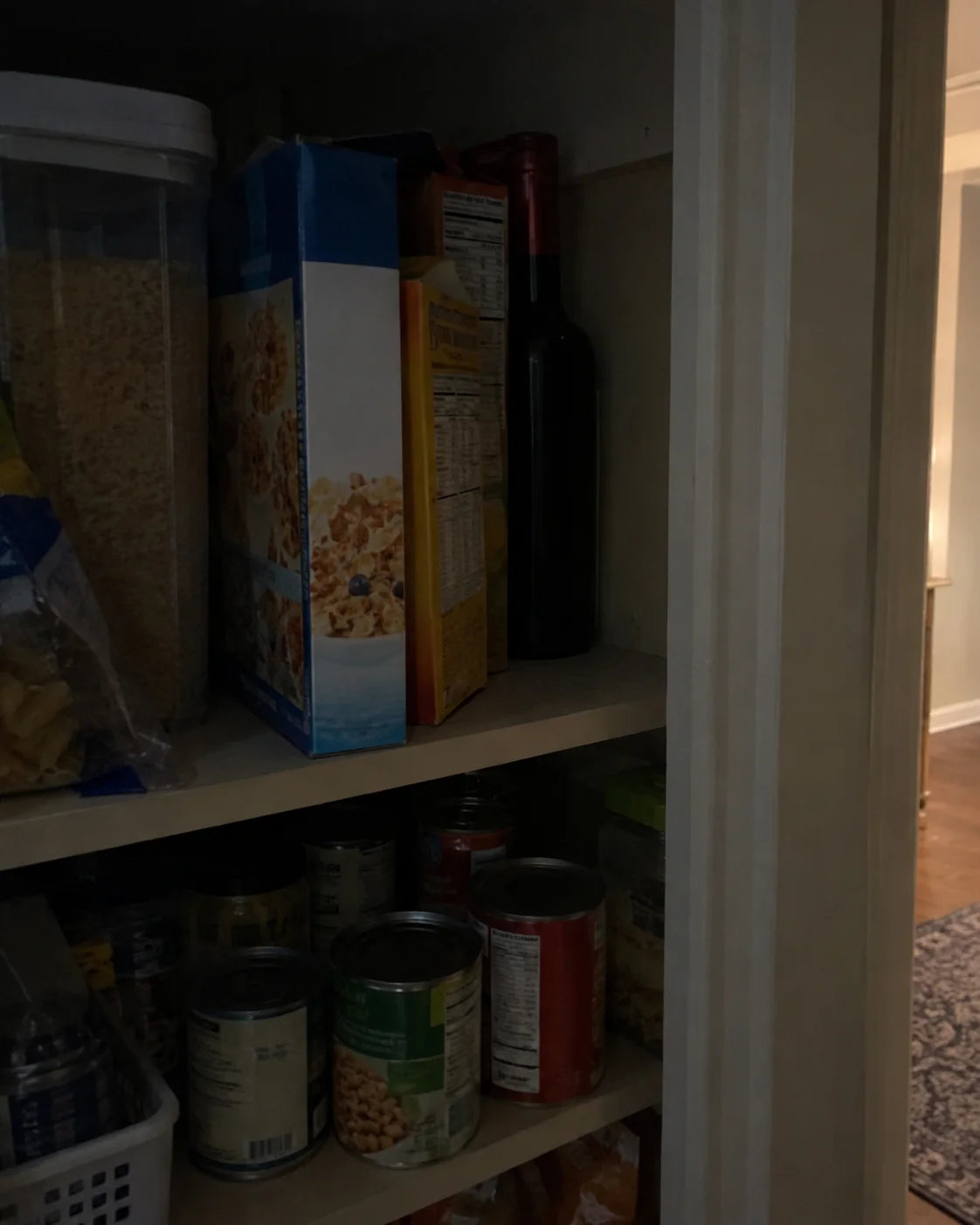 A wine bottle tucked behind cereal boxes and canned goods on a dim pantry shelf