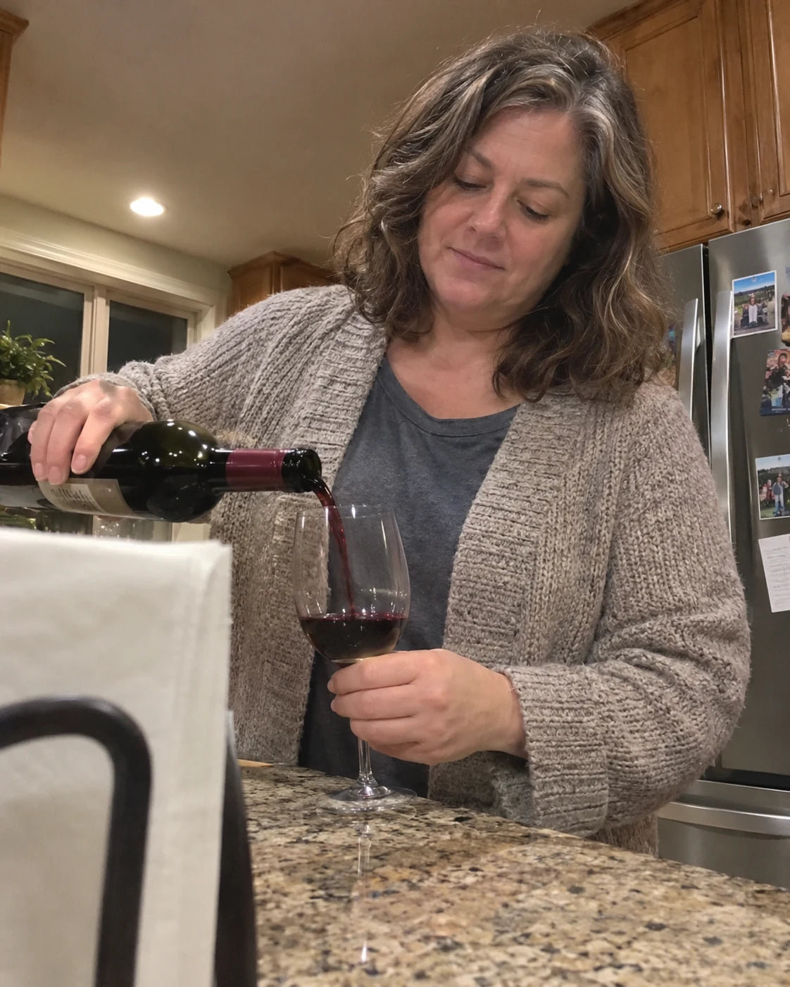 Woman pouring a glass of wine in her kitchen in the evening