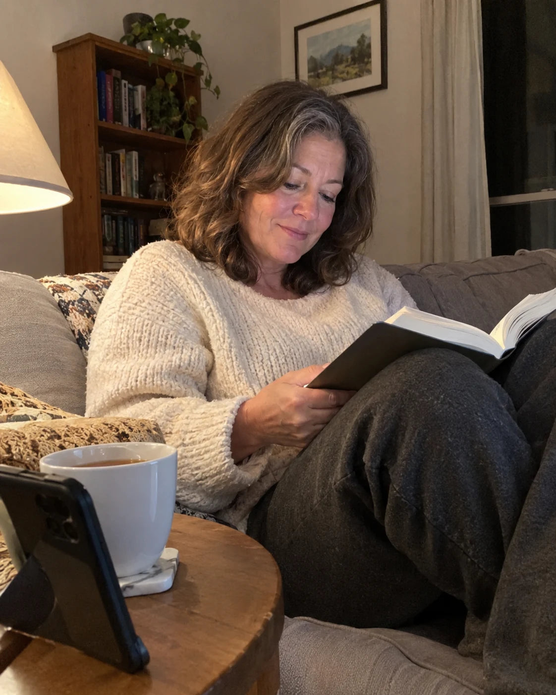 Woman relaxed on her couch in the evening with tea and a book, no wine
