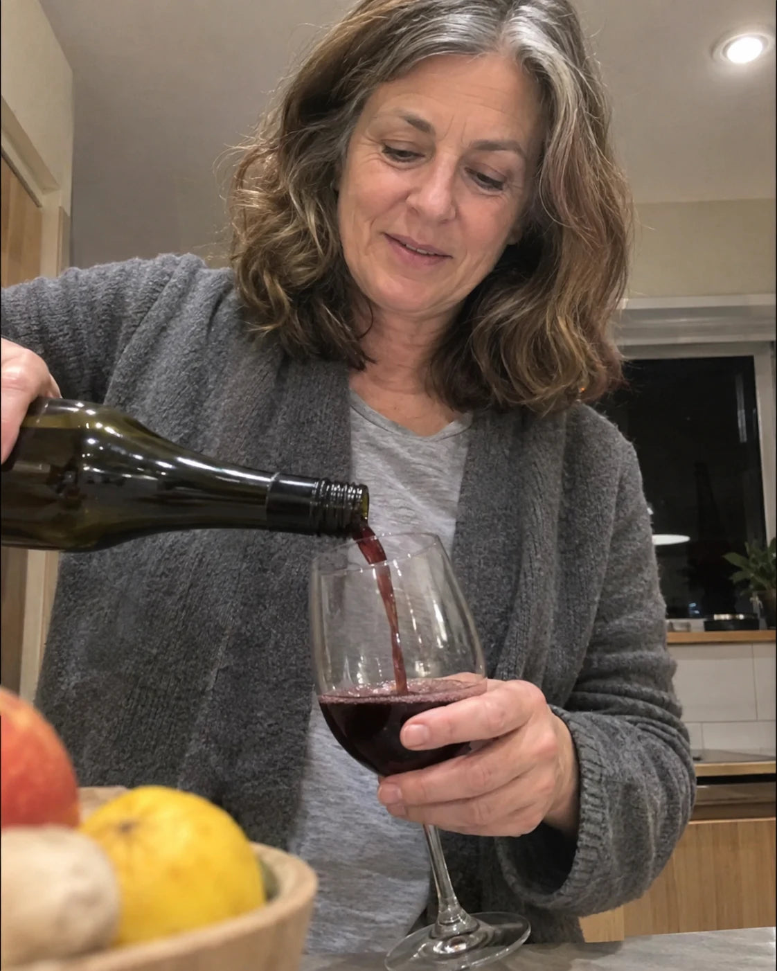Woman pouring a second glass of wine in her kitchen at night, candid phone video still