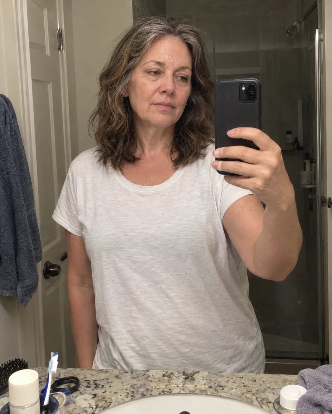 Woman's quiet mirror selfie at night in the bathroom, worn expression