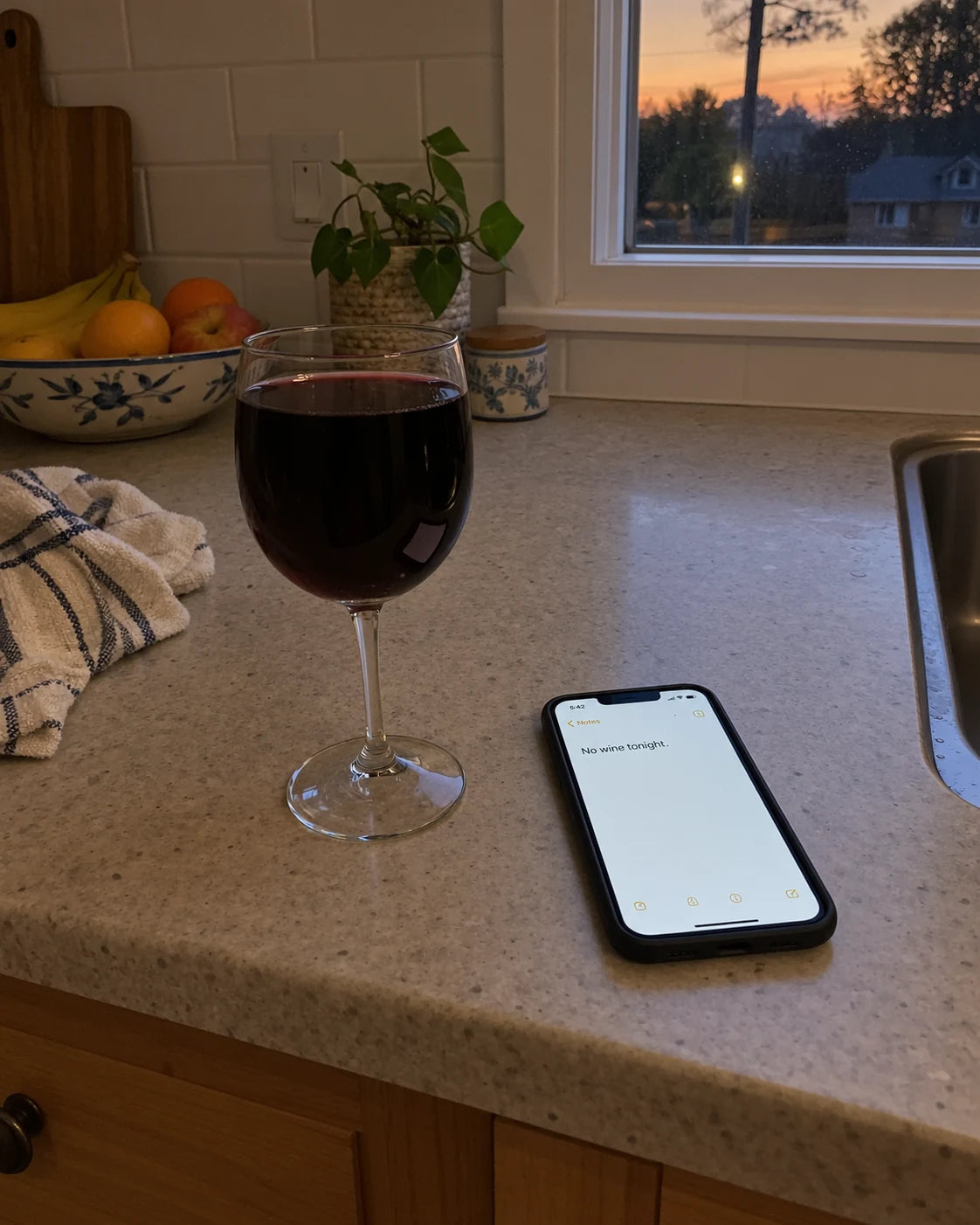 A poured glass of wine on the kitchen counter next to a phone showing a notes app reading No wine tonight