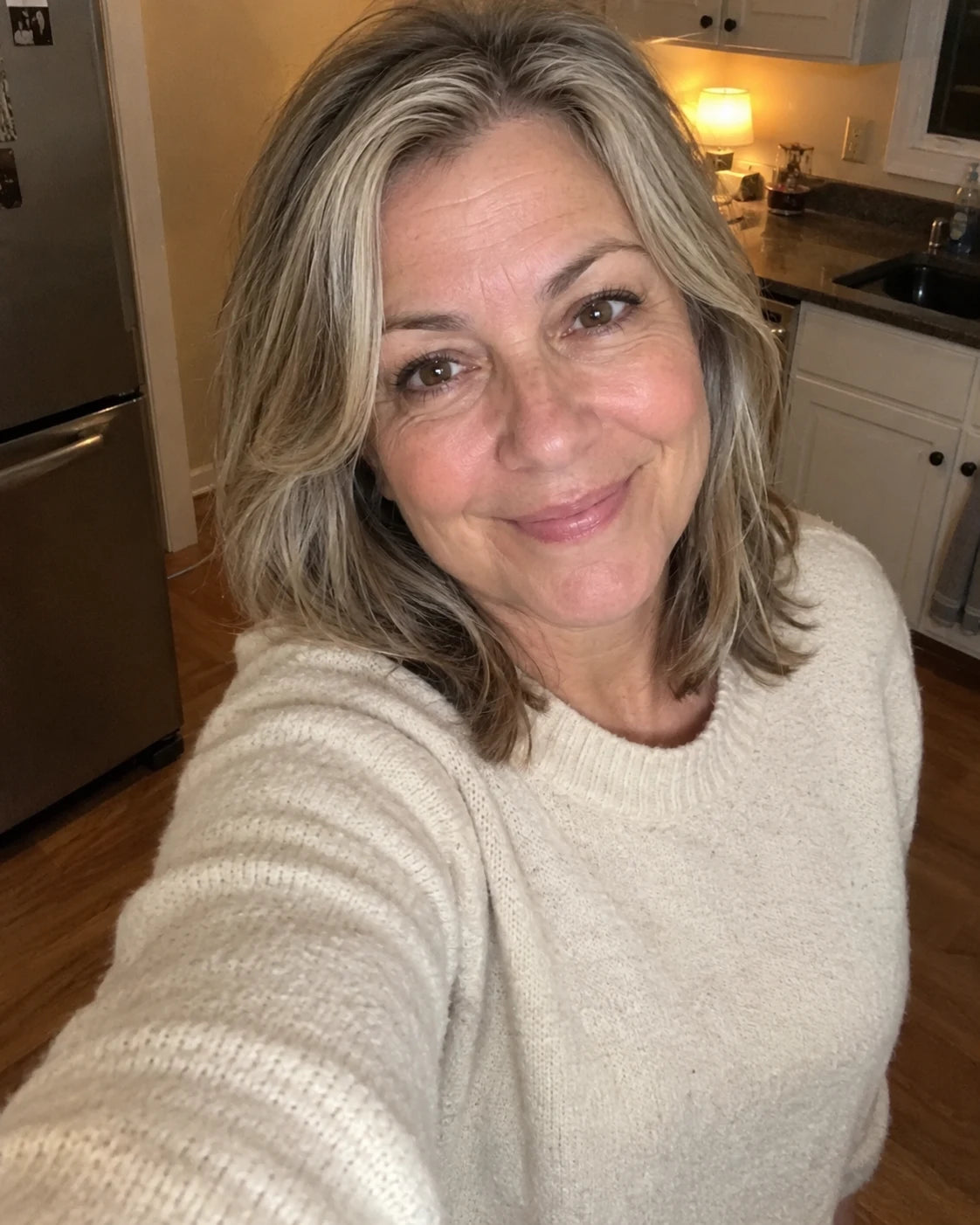 Calm, relaxed woman taking a smiling selfie in her kitchen in the evening