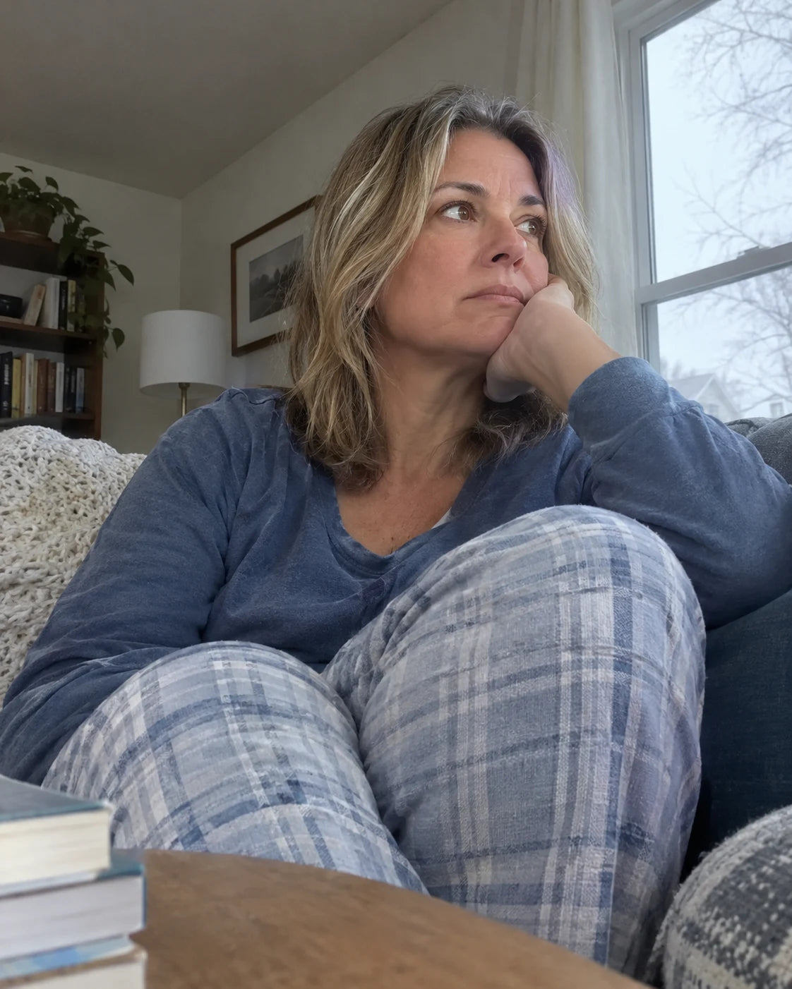 Woman sitting alone on the couch in pajamas on a quiet Saturday morning, looking out the window