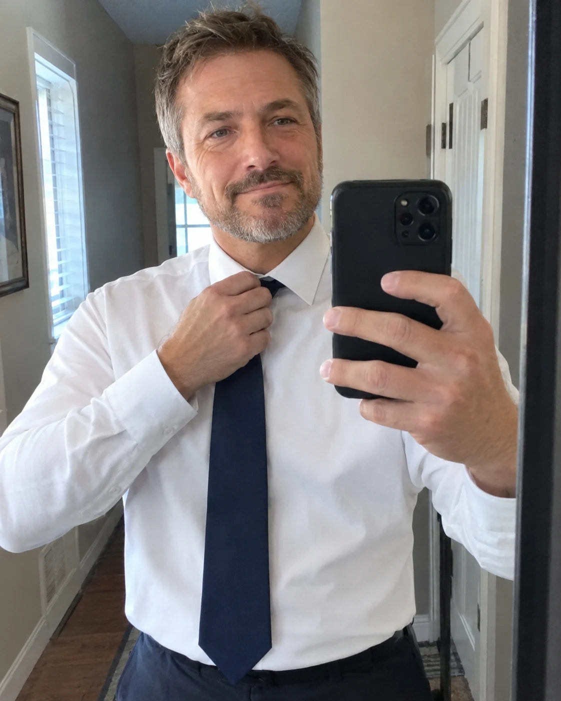 A man checking his tie in a mirror, fully dressed and composed, ready for work