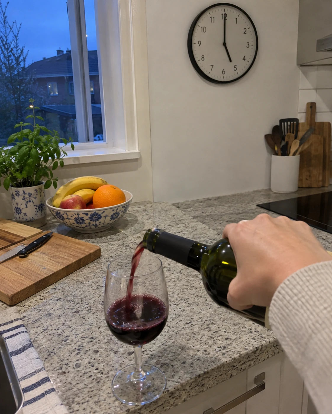 A hand pouring wine at 5pm without looking, next to a kitchen wall clock
