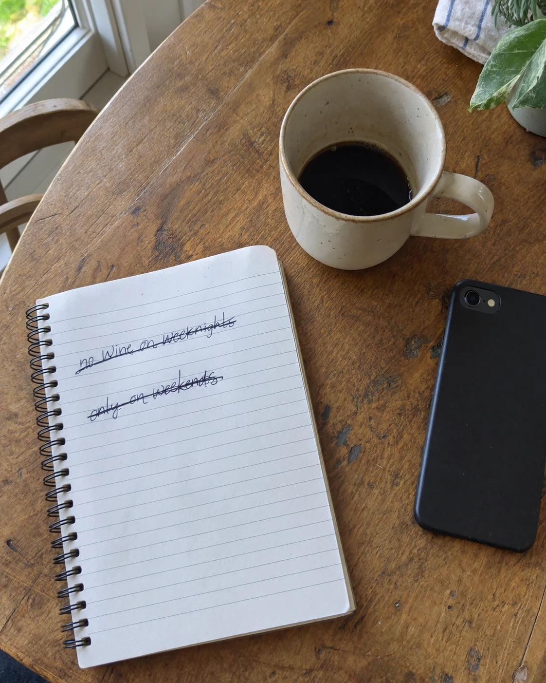 Notebook page with crossed-out drinking rules, coffee mug and phone on a kitchen table