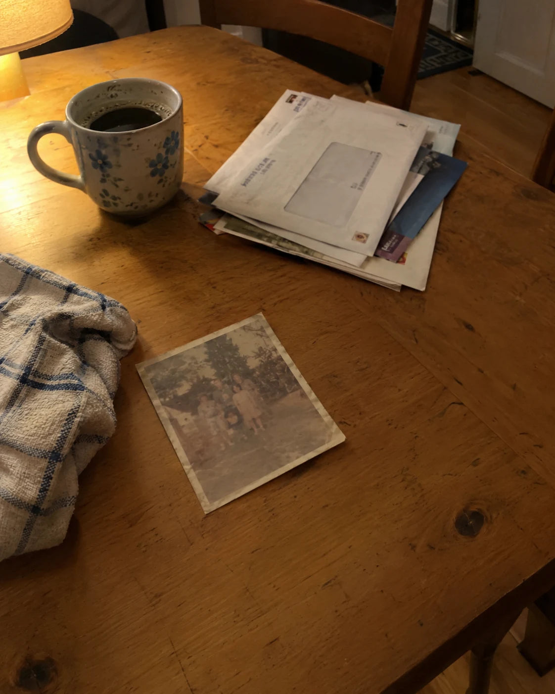An old family photo on a cluttered kitchen table next to unopened mail and a cold coffee