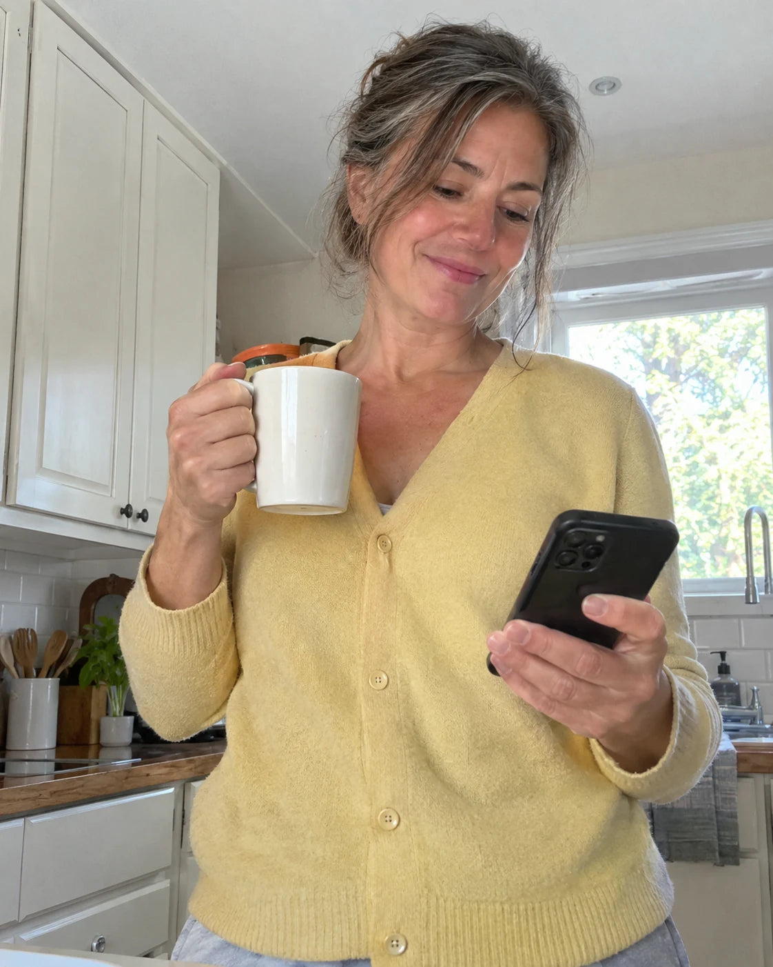 Woman smiling softly at her phone over morning coffee